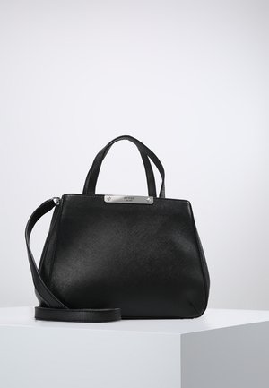 Sac à main Guess en cuir noir avec poignées courtes et bandoulière détachable sur un piédestal blanc.