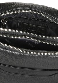 Interno di una borsa in pelle nera con scomparti con zip, caratterizzato da una superficie texturizzata e hardware argentato. Foderata in tessuto nero.