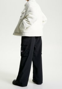 Creme fleecejakke med en afslappet pasform, krave og sidelommer, parret med løse sorte cargo-bukser med synlige forlommer.