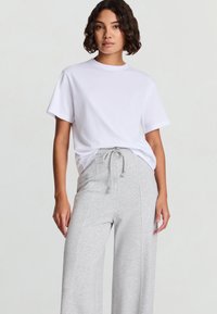 Maglietta bianca a maniche corte abbinata a pantaloni della tuta a gambe larghe di colore grigio chiaro, con vita a coulisse e tessuto morbido.
