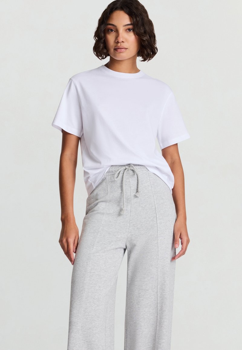 Maglietta bianca a maniche corte abbinata a pantaloni della tuta a gambe larghe di colore grigio chiaro, con vita a coulisse e tessuto morbido.