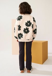 Kermitevärvi sweatshirt, millel on suur tume rohelise lillemuster, ribatud kaelus ja puhvitud varrukad; kombineeritud mustade laienevate pükste ja tossudega.