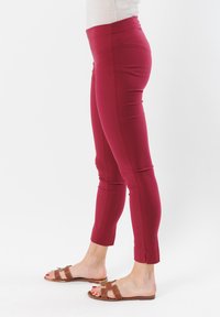Leggings bordeaux con design aderente, materiale elastico, vita media e lunghezza cropped, con cuciture laterali e texture liscia.