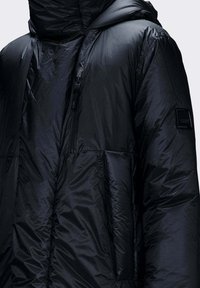 Giacca a piumino nera con cappuccio, con una texture trapuntata, cuciture orizzontali e tasca sul petto con cerniera. Decorata con una toppa del marchio.