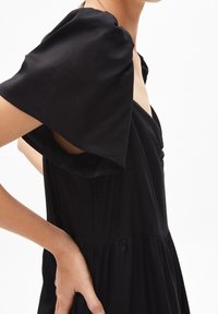 Černé šaty s krátkými rukávy s nařasenými rameny, výstřihem do V a přiléhavým živůtkem vedoucím ke nařasené, volně splývavé sukni. Hladká textura látky.