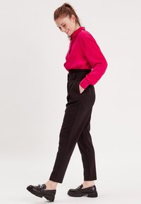 Magenta Langarmbluse, maßgeschneiderte schwarze hochtaillierte Hose und schwarze Slipper mit klobigen Sohlen, die mit einem Metallelement verziert sind.