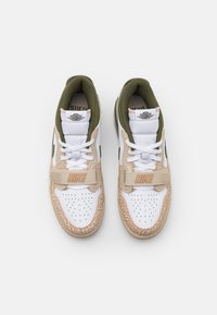 White sneakers with a beige and green design, featuring a textured toe, perforated upper, and a strap with "NIKE" branding.