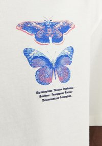 Bílá látka zobrazuje dva potisky motýlů; nahoře je hnědý a modrý můra, dole modrý motýl s červenými akcenty. Černý text pod tím.