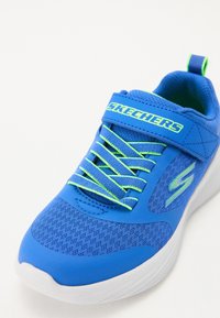 Blue athletic shoe featuring a textured mesh upper, neon green accents, elastic laces, and a white sole. Skechers branding visible on strap.
