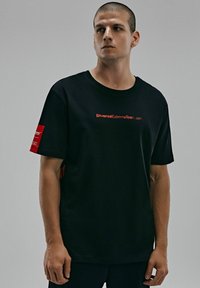 Czarna bawełniana koszulka z okrągłym dekoltem, krótkimi rękawami i czerwonym nadrukiem na przodzie oraz metką na rękawie.