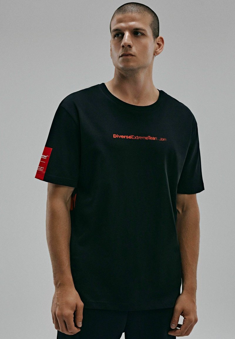 Czarna bawełniana koszulka z okrągłym dekoltem, krótkimi rękawami i czerwonym nadrukiem na przodzie oraz metką na rękawie.