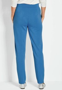 Blauwe, rekbare broek met een gladde textuur, een brede tailleband en taps toelopende pijpen, met twee achterzakken en zilveren platte schoenen.