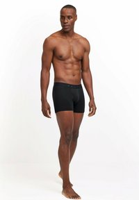 Schwarze Boxer Shorts mit elastischem Bund, der mit "FALKE" beschriftet ist. Hergestellt aus glattem Stoff, körpernahem Design und in mittellanger Ausführung bis zur Oberschenkelmitte.