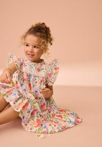 Floral jurk met gerimpelde mouwen en kantdetails, met roze, blauwe en oranje bloemen op een crèmekleurige achtergrond. Lichtgewicht stof, kniehoogte.