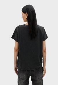 Camiseta negra de manga corta con un ajuste holgado, hecha de un tejido suave. Presenta un cuello redondo y un dobladillo ligeramente curvado. Combinada con jeans grises.