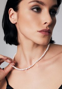 Szereg małych, okrągłych białych pereł noszonych na szyi, charakteryzujących się gładką teksturą i jednolitym kształtem, podkreślających linię szyi.