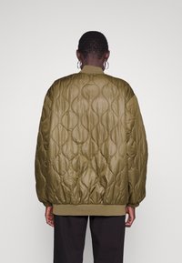 Oliwkowo zielona pikowana kurtka o gładkiej fakturze, z prążkowanymi mankietami i okrągłym dekoltem, zdobiona wzorzystym przeszyciem.