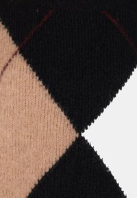 Tessuto lavorato a maglia con motivo a diamante che presenta sezioni nere e beige, con una texture morbida e una sottile linea di accento rossa.