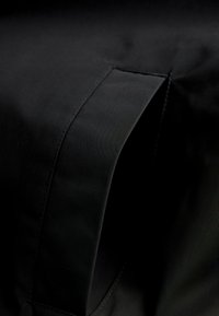 Gros plan d'un vêtement en tissu noir présentant une ouverture de poche inclinée cousue avec des détails de couture visibles.