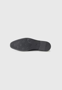 Schwarze Gummisohle mit kreisförmigen Grip-Mustern und einem glatten Zehenbereich. Die Ferse ist leicht strukturiert für zusätzlichen Halt.