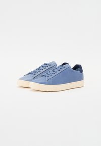 Blue leather sneakers with a smooth texture, featuring a cream rubber sole, lace-up design, and minimalistic accents.