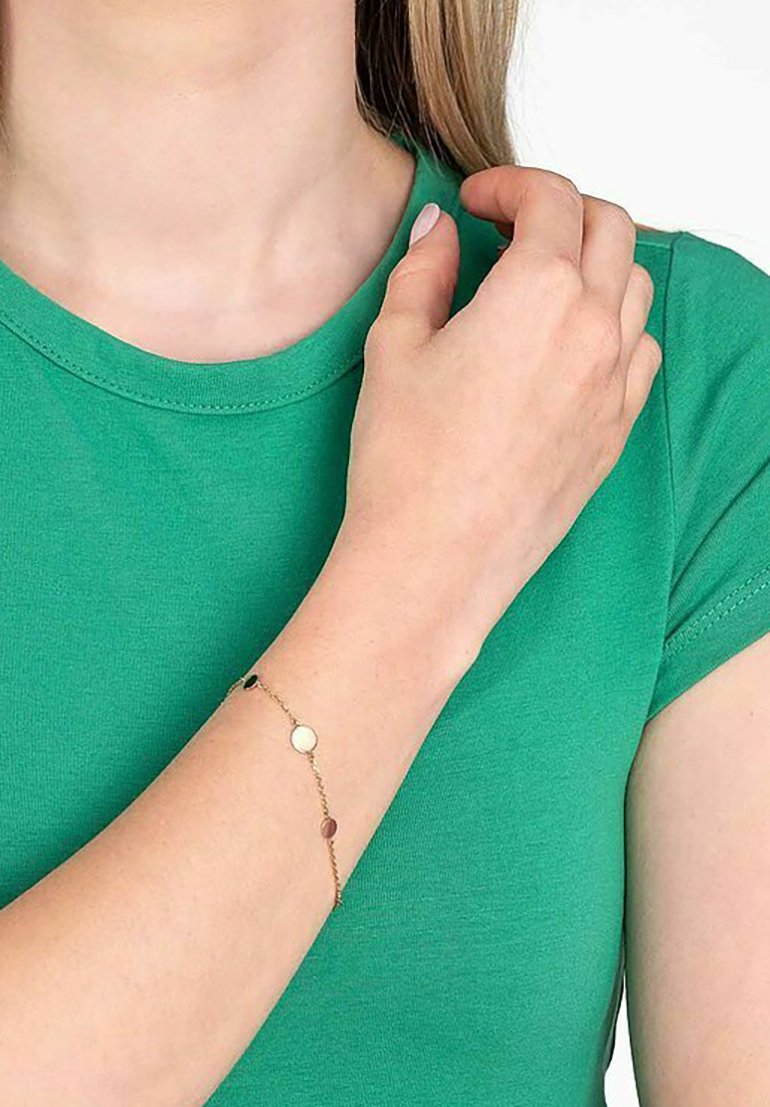 Gouden kettingarmband met ronde en ovale schijfjes in afwisselende kleuren, gedragen om een lichte huidarm tegen een groene shirt.