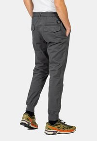 Pantalones de chándal grises con una cinturilla elástica y dos bolsillos traseros. Llevados con zapatillas de running verdes y naranjas que tienen una suela texturizada.
