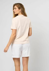 Lys ferskenfarget t-skjorte med korte ermer og avslappet passform, kombinert med hvite linshorts med oppbrett. Glatt tekstur, enkelt design.