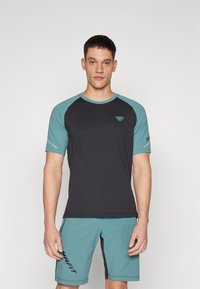 Pánský sportovní outfit skládající se z černého trička s aquamarínovými rukávy a logem, doplněný aquamarínovými šortkami s černou grafiku značky. Hladký materiál.