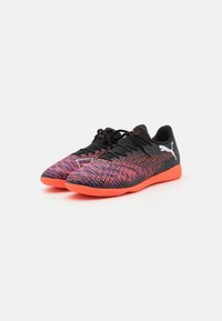 Buty sportowe Puma z czarną dzianiną górną w wielokolorowy zygzakowy wzór, czarnymi sznurowadłami i jasnopomarańczową podeszwą. Minimalne logo po bokach.