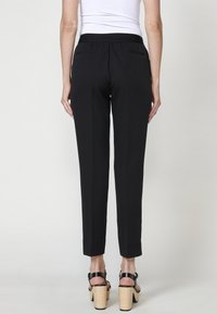 Pantalon noir ajusté avec une jambe étroite, une taille élastique et deux poches arrière. Assorti à des talons noirs à lanières avec une épaisse plateforme tressée.