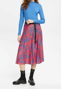 Röd och blåmönstrad plisserad kjol med ett svart bälte, parat med en blå långärmad topp och svarta blanka skor.