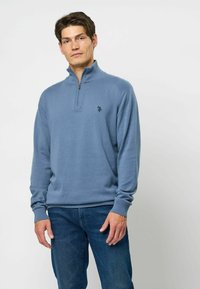 Kék pulóver, negyedcipzáros gallérral, bordás mandzsettákkal és szegéllyel. A mellkasán egy kis fekete logó található. Puha anyagból készült.