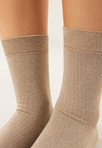 Calze fino al ginocchio di colore beige chiaro con una texture a coste e fili sottili scintillanti, dotate di un polsino rinforzato e una finitura liscia.