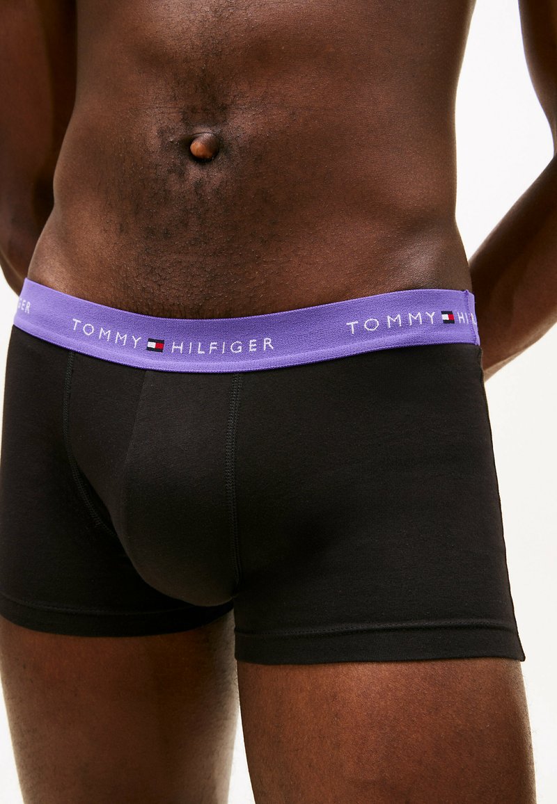 Boxers noirs avec une ceinture lavande affichant le texte et le logo "TOMMY HILFIGER". Le tissu semble doux avec un ajustement confortable.