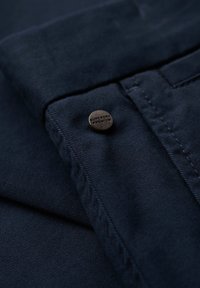 Granatowy materiał o teksturowanym splocie z metalowym guzikiem z grawerunkiem "Superdry Premium", przymocowanym do złożonego brzegu.