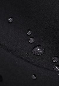 Tessuto nero con gocce d'acqua visibili, che mette in evidenza una trama liscia e una leggera lucentezza. Vista ravvicinata che sottolinea la resistenza all'acqua del materiale.