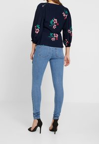 Marinebluse med blomsterbroderi, puffærmer, parret med lyseblå stramme jeans og sorte højhælede sko.
