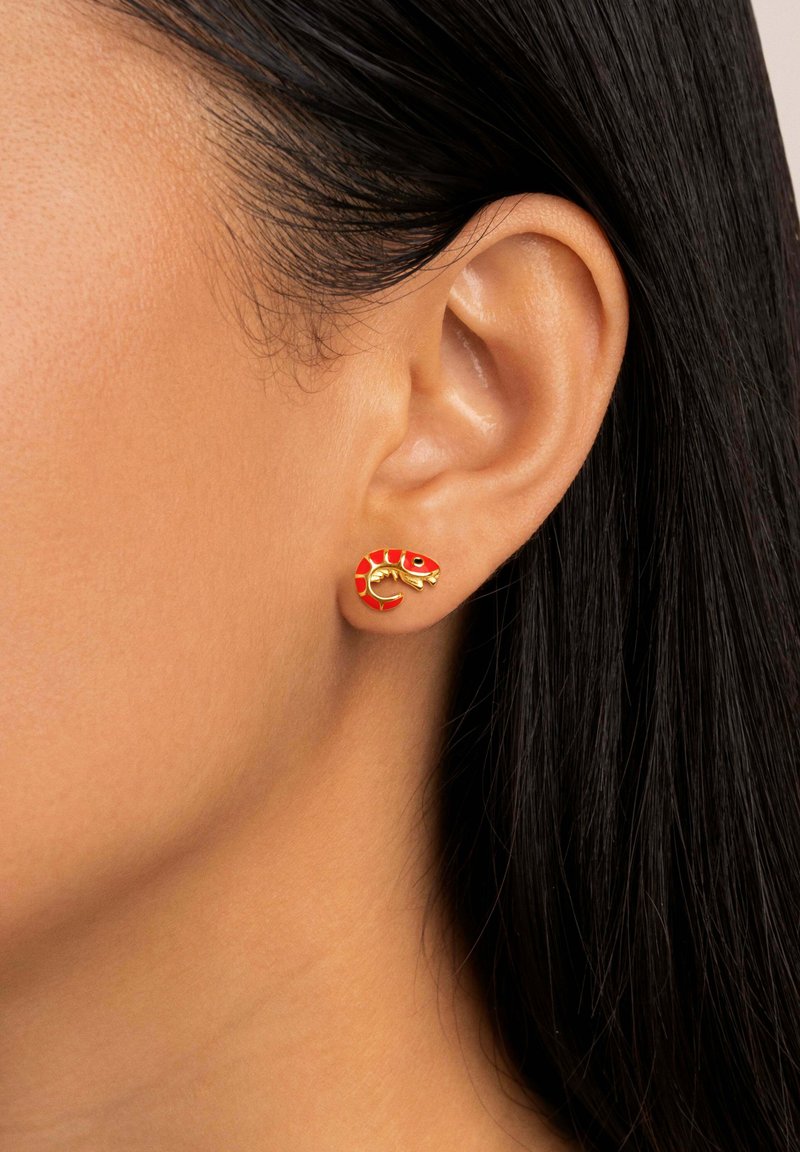 Boucles d'oreilles dorées en forme de serpent, avec une finition en émail rouge et des accents noirs, présentées sur l'oreille d'un modèle.