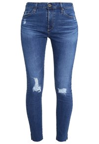 Jeans ajustados de mezclilla azul oscuro con acabado desgastado, que presentan dos desgastes en las rodillas y un diseño estándar de cinco bolsillos. Cierre con botón plateado.