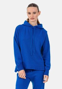 Sweat à capuche bleu en tissu tricoté. Présente une coupe décontractée, des manches longues, une poche kangourou avant, ainsi que des poignets et un ourlet côtelés.