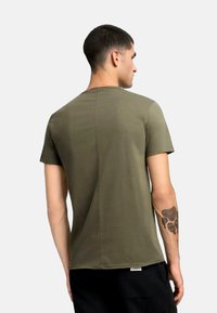 Tricou scurt cu mânecă scurtă de culoare verde oliv, cu guler rotund, având un detaliu de cusătură centrală, țesătură moale și etichetă la marginea inferioară.