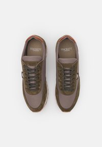 Ein Paar braune und olivgrüne Sneaker von Hackett London mit Wildleder- und Mesh-Panels, dunkelgrünen Schnürsenkeln und weißen Gummisohlen auf einem weißen Hintergrund.