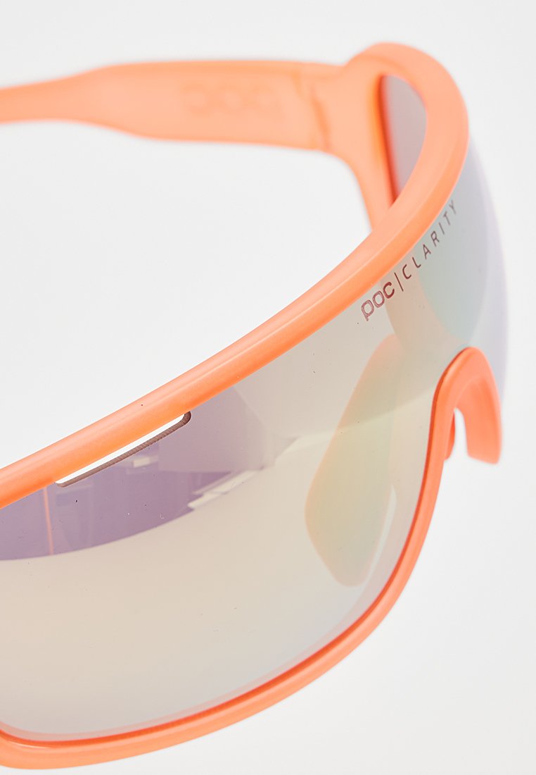 Pomarańczowe sportowe okulary przeciwsłoneczne z zaokrąglonym designem. Posiadają błyszczące, lustrzane soczewki oraz lekką plastikową oprawę. Widoczne logo POC Clarity.