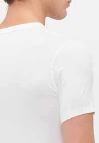 Vue arrière d'une personne portant une chemise blanche ajustée à manches courtes avec des coutures visibles sur les épaules et les manches.