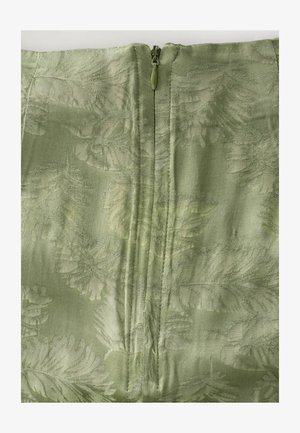 Tissu vert avec un motif de feuilles texturé, présentant une fermeture éclair centrée à l'arrière. Matériau lisse et semi-transparent avec un éclat subtil.