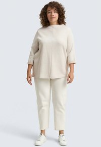 Ljust beige texturerad topp med trekvartsärmar, kombinerad med krämfärgade smalnande byxor och vita sneakers, med en avslappnad silhuett.