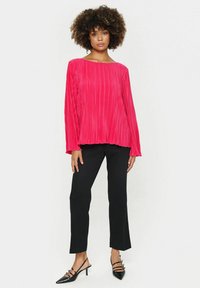 Rdeč plisiran dolg rokav z širokim ovratnikom, v kombinaciji s črnimi ravnimi hlačami in črnimi veznimi čevlji z nizko peto.