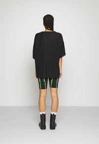 Top oversized in pleated nero abbinato a pantaloni ciclistici a strisce nere e verdi. Dettagli aggiuntivi includono stivali alla caviglia neri e calzini bianchi.