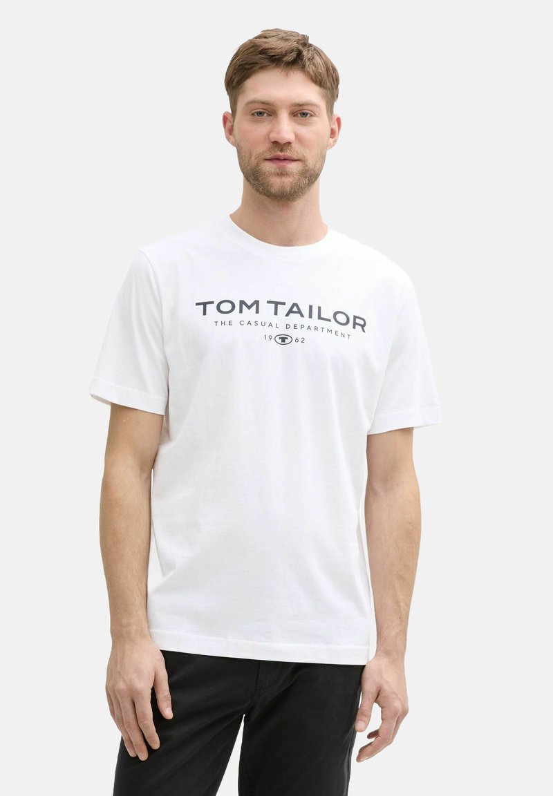Weißes Baumwoll-T-Shirt mit der Aufschrift "TOM TAILOR THE CASUAL DEPARTMENT 1962" in dunkelblau über der Brust. Kurze Ärmel und Rundhalsausschnitt.